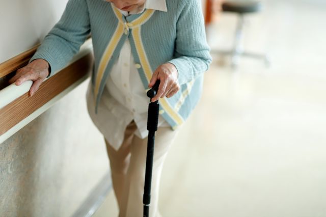 Una mujer de edad avanzada intentando caminar con bastón.