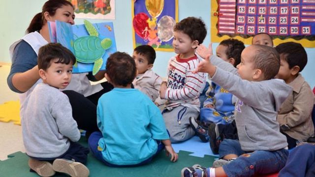 Educadora e crianças lendo um livro infantil em creche municipal
