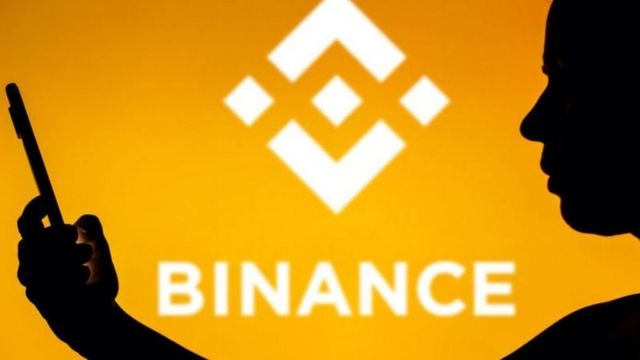 Un hombre mira a un celular frente a un fondo que dice Binance.