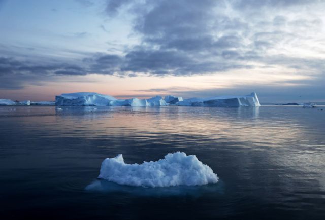 Masa de hielo flotando en el océano con un glaciar de fondo.