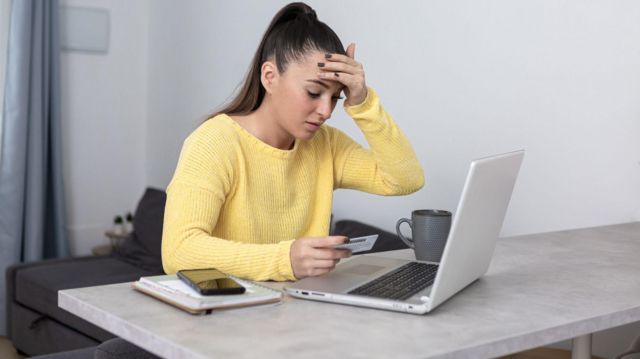 Mulher olhando com preocupação para computador e segurando cartão de crédito