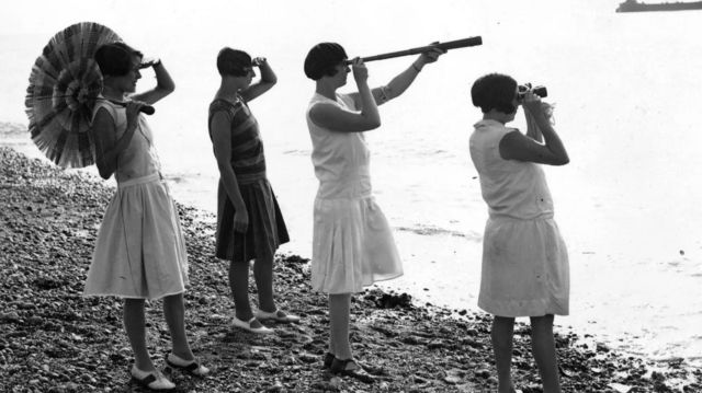 Foto antiga de mulheres na praia olhando com lunetas