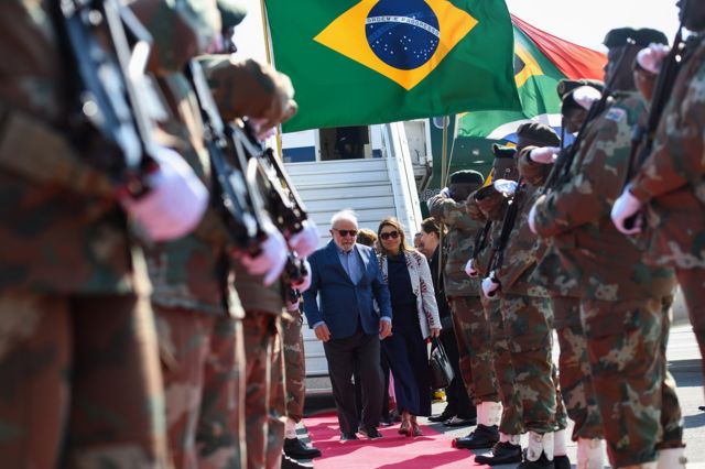 Lula e a primeira-dama caminhando em tapete vermelho ao descer de avião 