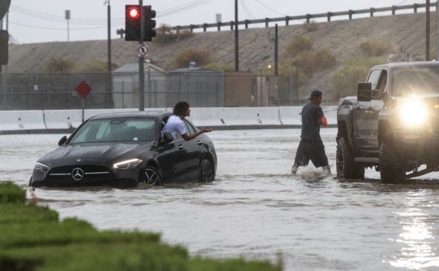 Un conductor cuyo automóvil quedó parado en una avenida inundada pide ayuda a un transeúnte durante la tormenta tropical Hilary en Coachella, California.