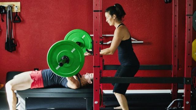 Mulher ajuda homem em exercício com barra