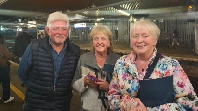 Three people standing on a train station platform