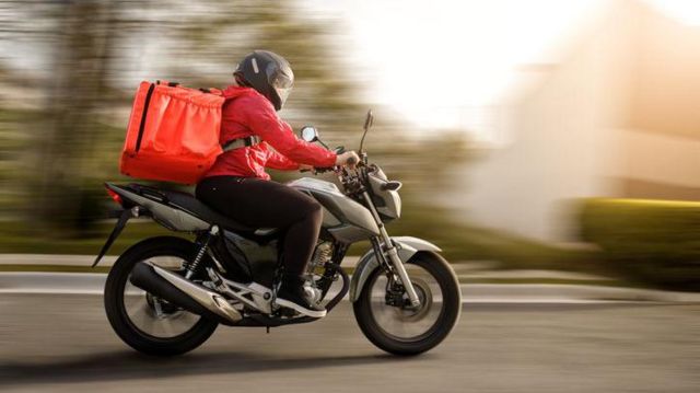 pessoa dirige moto com mochila de entrega de alimentos