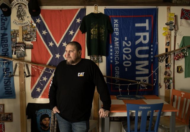 Homem em frente a bandeiras da confederação americana e de Trump