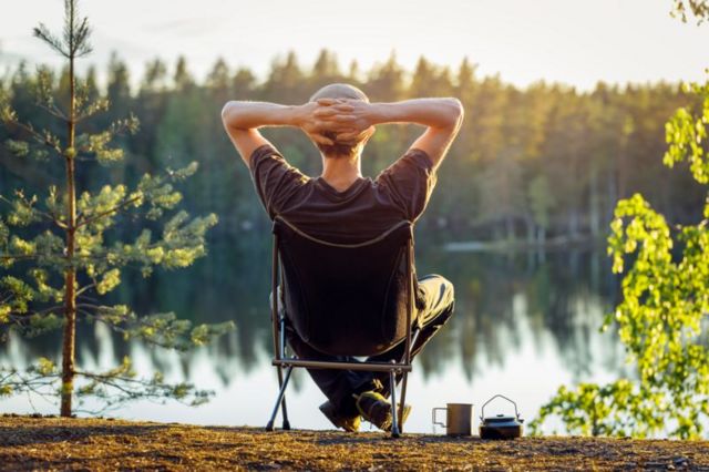 Homem de costas sentado em cadeira à beira de um lago aproveitando paisagem ao ar livre 
