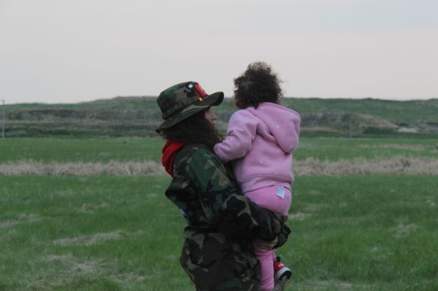 Cambria Harris com filha pequena no colo (de costas), em área de gramado con su hija en brazos.