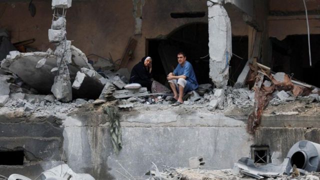 Palestinos sentam-se entre os escombros de um prédio residencial danificado, após ataques israelenses, na Ccidade de Gaza