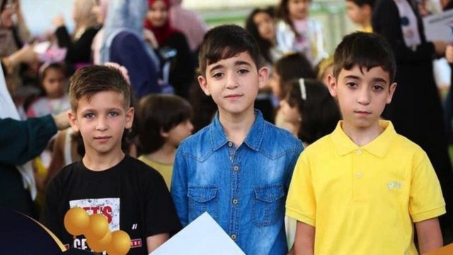 Três meninos recebendo prêmios na escola