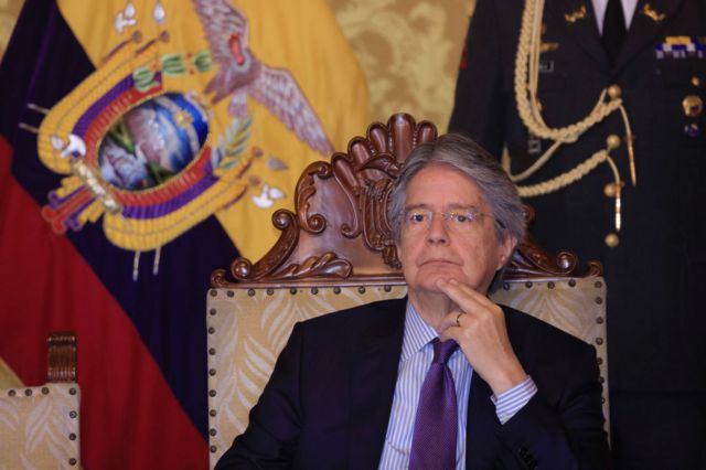 El presidente ecuatoriano Guillermo Lasso sentado con una bandera nacional al lado.