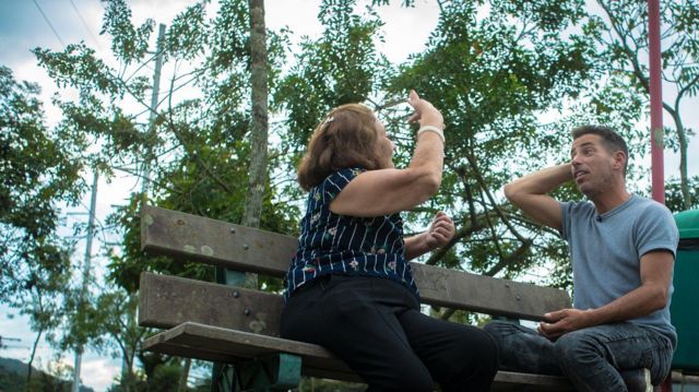 Mãe e filho conversando em banco de praça; ela gesticula