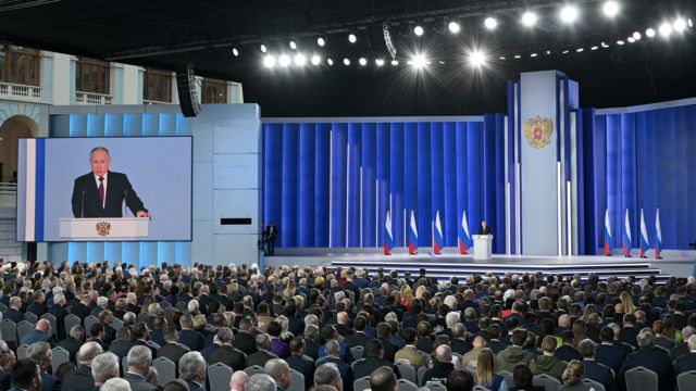 Putin discursa diante de plateia, com telão ao lado