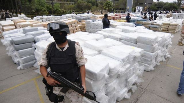 Policial em frente a sacos de drogas