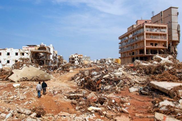Dos personas pasan por encima de una ruinas en Derna.