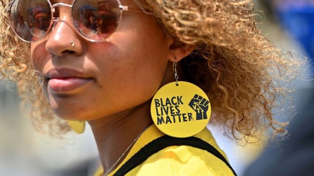 Une femme noire avec une boucle d'oreille Black Lives Matter regarde la camera