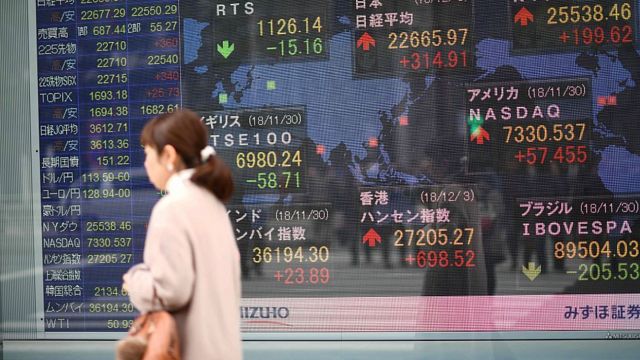 Mujer frente a un tablero del valor de acciones en la bolsa japonesa