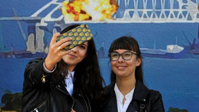 Hai phụ nữ ở Kyiv chụp ảnh trước hình một chiếc tem Ukraine mới phát hành, cho thấy hình ảnh cầu Crimea đang cháy. 