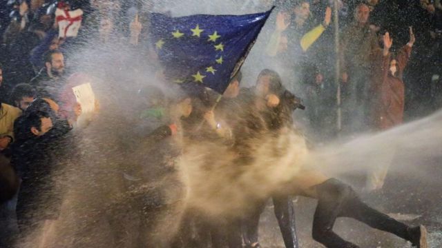 Участники протеста с флагом Европейского Союза обрызгиваются водометом. 7 марта 2023 год