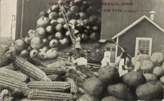 Várias mulheres e um homem do lado de fora de um celeiro cheio de cebolas gigantes, milhos e batatas, em Waupun, Wisconsin, 1912.