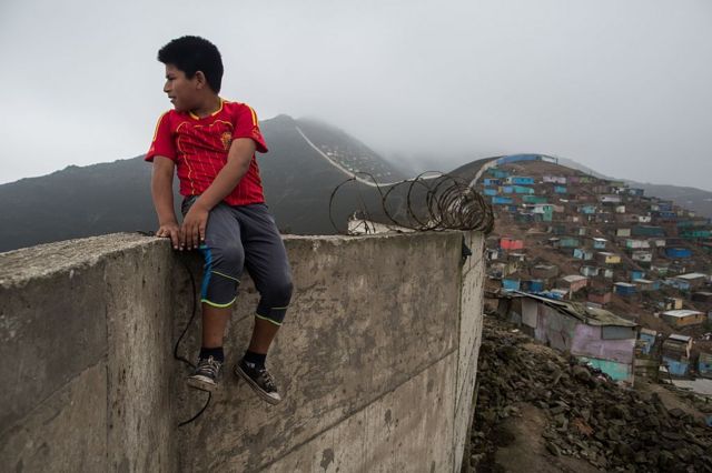 Un niño sentado en un muro que separa un barrio pobre del resto de Lima.