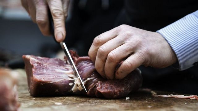 Mão de alguém cortando carne sobre uma tábua