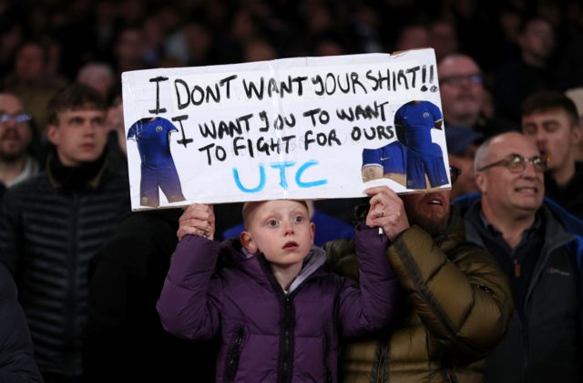 A young Chelsea fan with a banner criticising players efforts