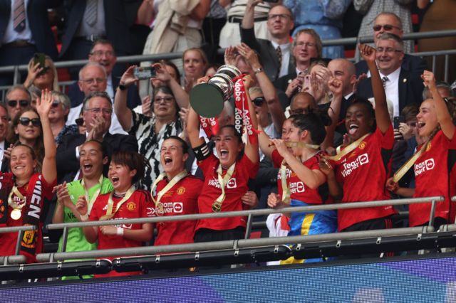 Katie Zelem of Manchester United lifts the Adobe Women's FA Cup trophy as she celebrates with teammates on the balcony after the Adobe Women's FA Cup Final match between Manchester United and Tottenham Hotspur