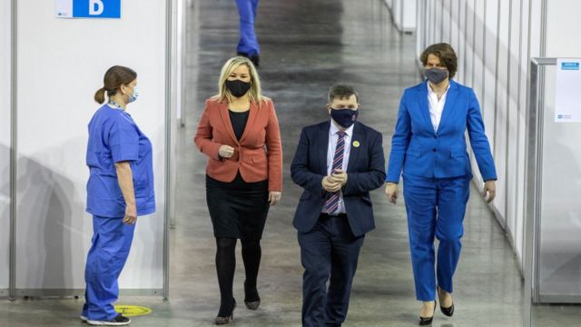 Northern Ireland's First Minister Arlene Foster (R) and Deputy First Minister Michelle O'Neill walk with Health Minister Robin Swann as they visit the SSE Arena which has been converted into a temporary Covid-19 vaccination centre, in Belfast, Northern Ireland on March 29, 2021.