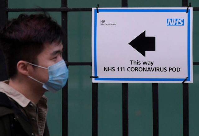 Person walks past sign saying 'This way Coronavirus Pod'