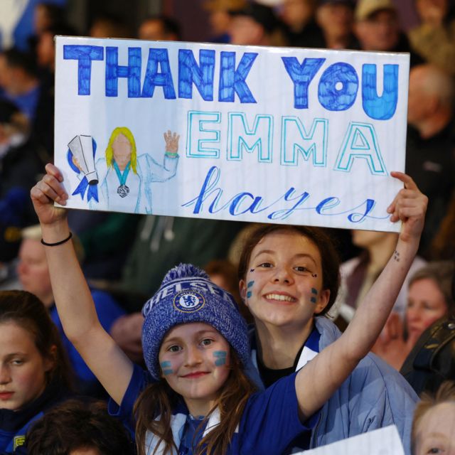 A young fan holds a sign saying 'Thank you Emma Hayes'