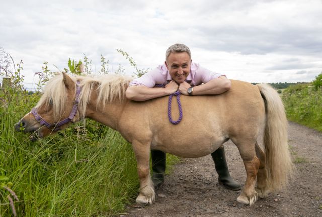 Alex Cole-Hamilton leaning on a tan pony