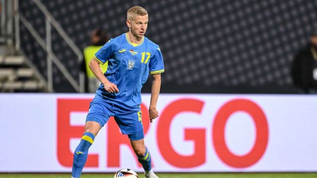 Ukraine defender Oleksandr Zinchenko playing for his country.  He is in action with the ball at his feet.  Wearing a blue strip with yellow trimming.