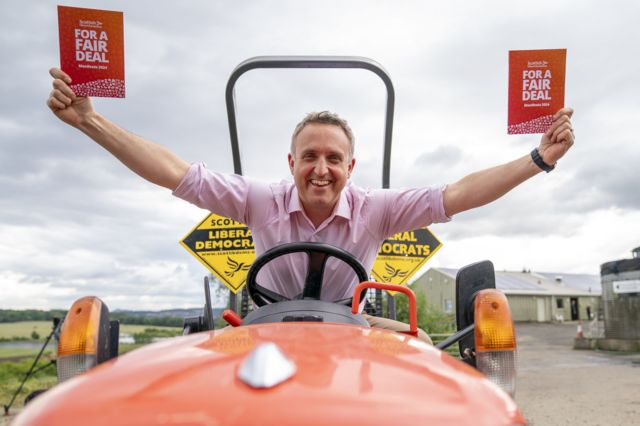 Alex Cole-Hamilton rides a red tractor while holding the newly launched manifesto