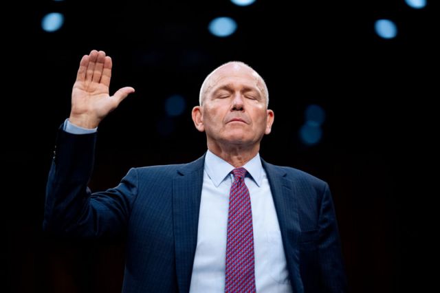 Boeing CEO Dave Calhoun is sworn in at a hearing, with one hand raised and his eyes closed.