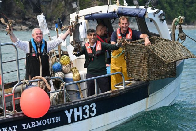 Prime Minister Rishi Sunak (centre) and Conservative Parliamentary Candidate for Torridge and Tavistock Sir Geoffrey Cox (left), ride on a boat in the harbour at Clovelly as they collect lobster pots, during a visit to North Devon, while on the General Election campaign trail. Picture date: Tuesday June 18, 2024.