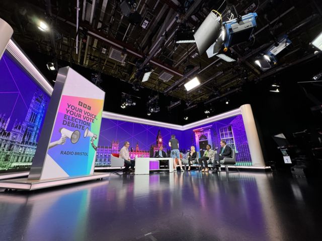 View inside the studio with candidates sat on chairs with a purple background