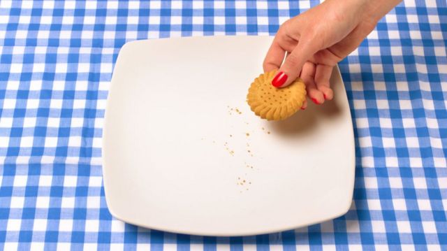 Woman with painted red nail takes last biscuits from a plate on a blue gingham tablecloth