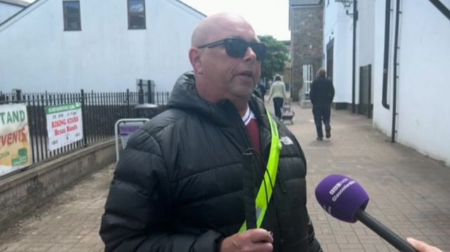 John in Coleford stood in a street with a purple microphone in front of him