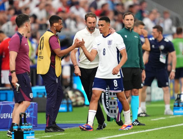 Trent Alexander-Arnold shakes hands with a member of the England coaching staff after being replaced against Denmark