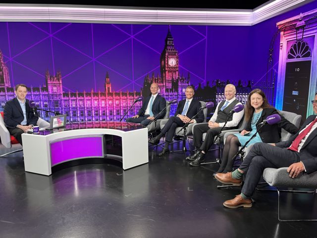 Candidates sitting in a purple studio on grey chairs