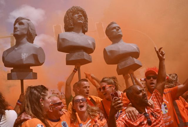 Netherlands fans are seen holding statues of Johan Cruyff, Ruud Gullit and Marco van Basten during a march