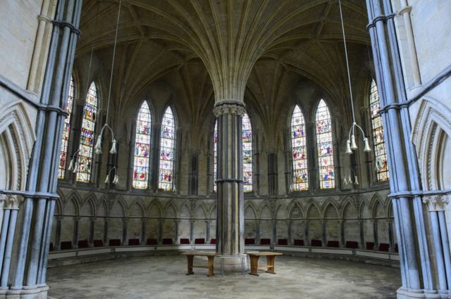 Empty interior of Lincoln Cathedral's Chapter House with stained glass windows, stone ribs and two seats next to the middle column