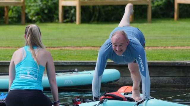 Lib Dem leader Ed Davey on all fours with one leg in the air on a blue paddleboard