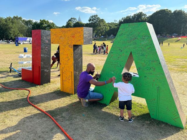 A man crouches with a child next to huge letters that spell out ATL - part of a Juneteenth celebration in Atlanta's Piedmont Park