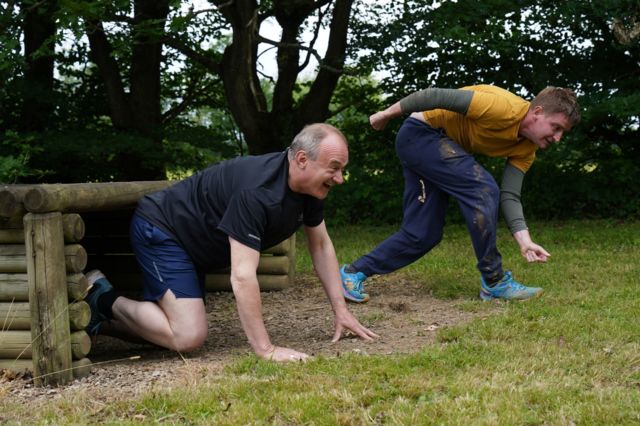 Ed Davey crawls out of a wooden structure as part of an assault course
