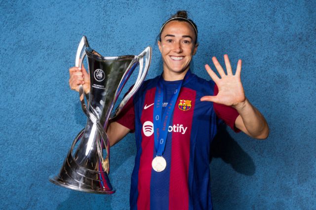 Lucy Bronze puts up five fingers as she holds the Women's Champions League trophy