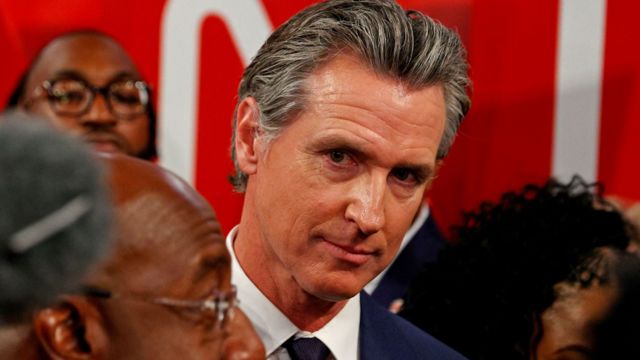 California Gov. Gavin Newsom looks on as Sen. Warnock answers a question from the media in the debate spin room.